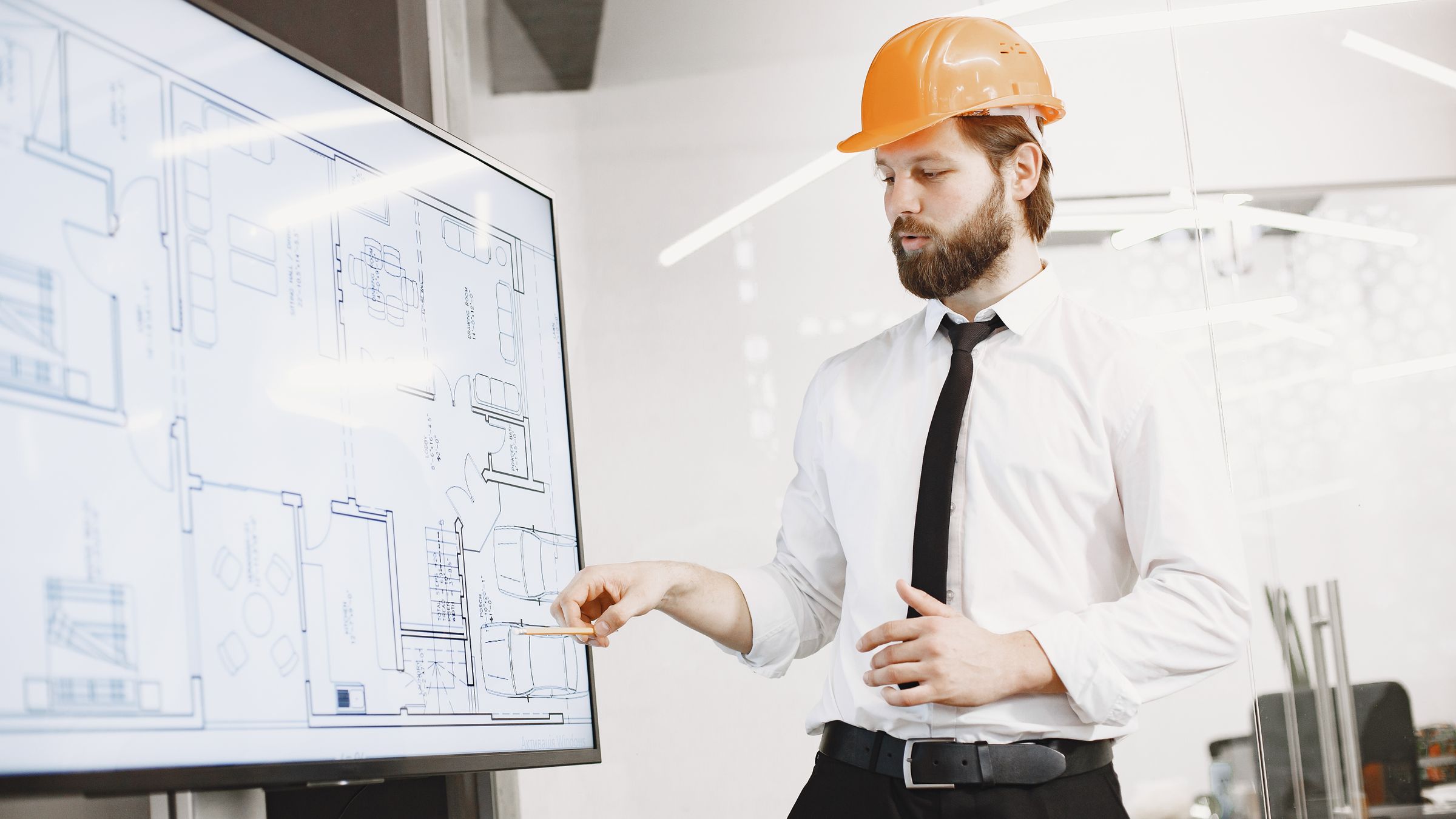 A project manager in a hard hat reviewing construction drawings on a screen in an office